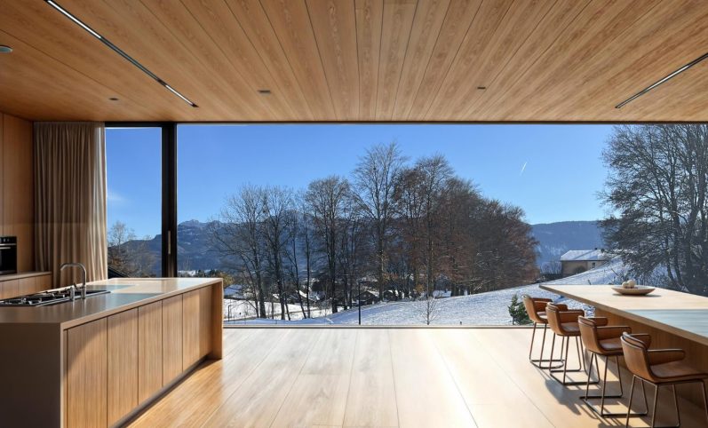 Moderne Küche mit Holzdecke und Blick auf schneebedeckte Landschaft und See.